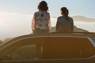 Duas pessoas em cima de um carro chevrolet observando o pôr-do-sol